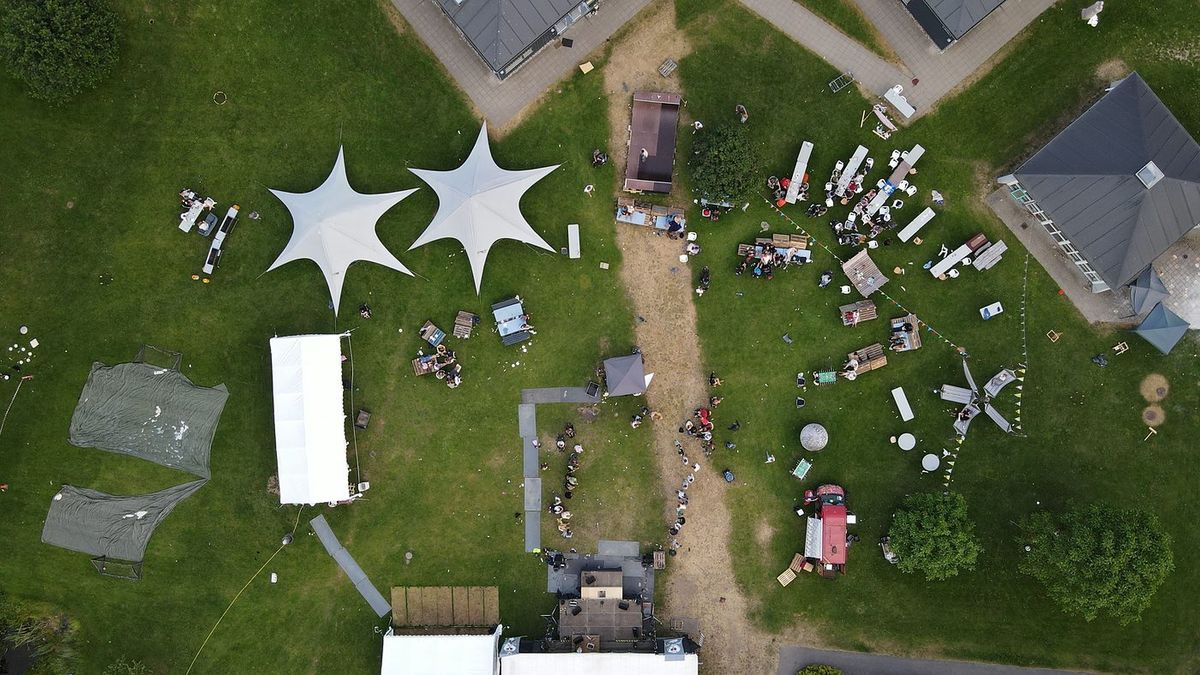Drohnenaufnahme eines Outdoor-Events mit Zelten und Besuchern auf einer Wiese