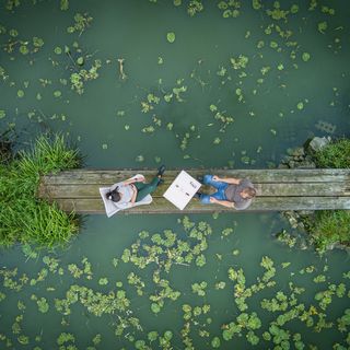 Drohnenaufnahme Saarland: Zwei Personen auf einem Steg über einem Teich senkrecht von oben