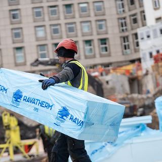 Industriefotografie Saarland: Arbeiter trägt Ravatherm Dämmplatten über die Baustelle