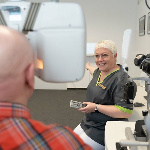 Praxisfotografie Saarland: Mitarbeiterin erklärt einem Patienten die Untersuchung am Augenmessgerät